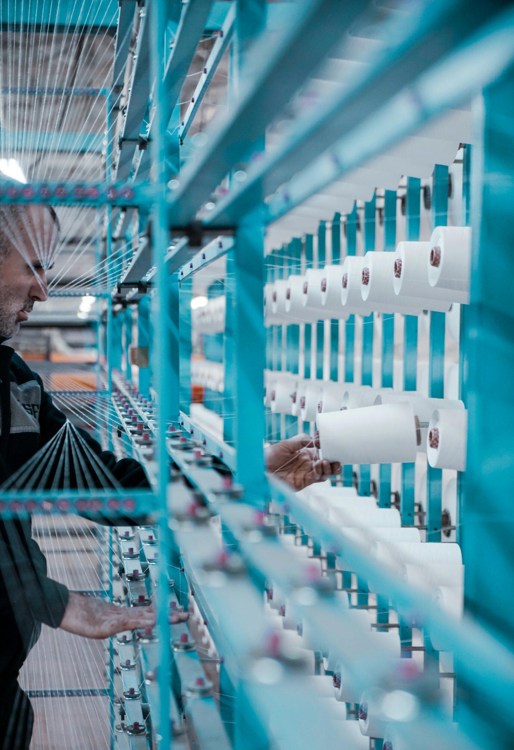 A textile factory worker inspects spools of thread on modern industrial machinery.